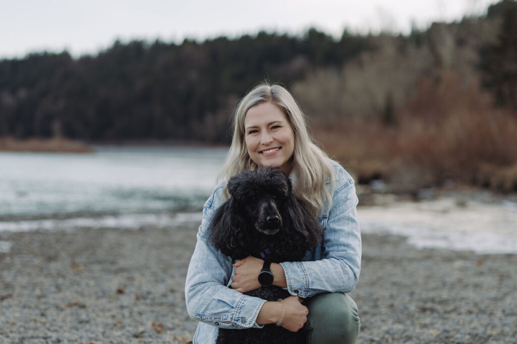 A photo of Marie hugging her black poodle, Vivian, at a lake